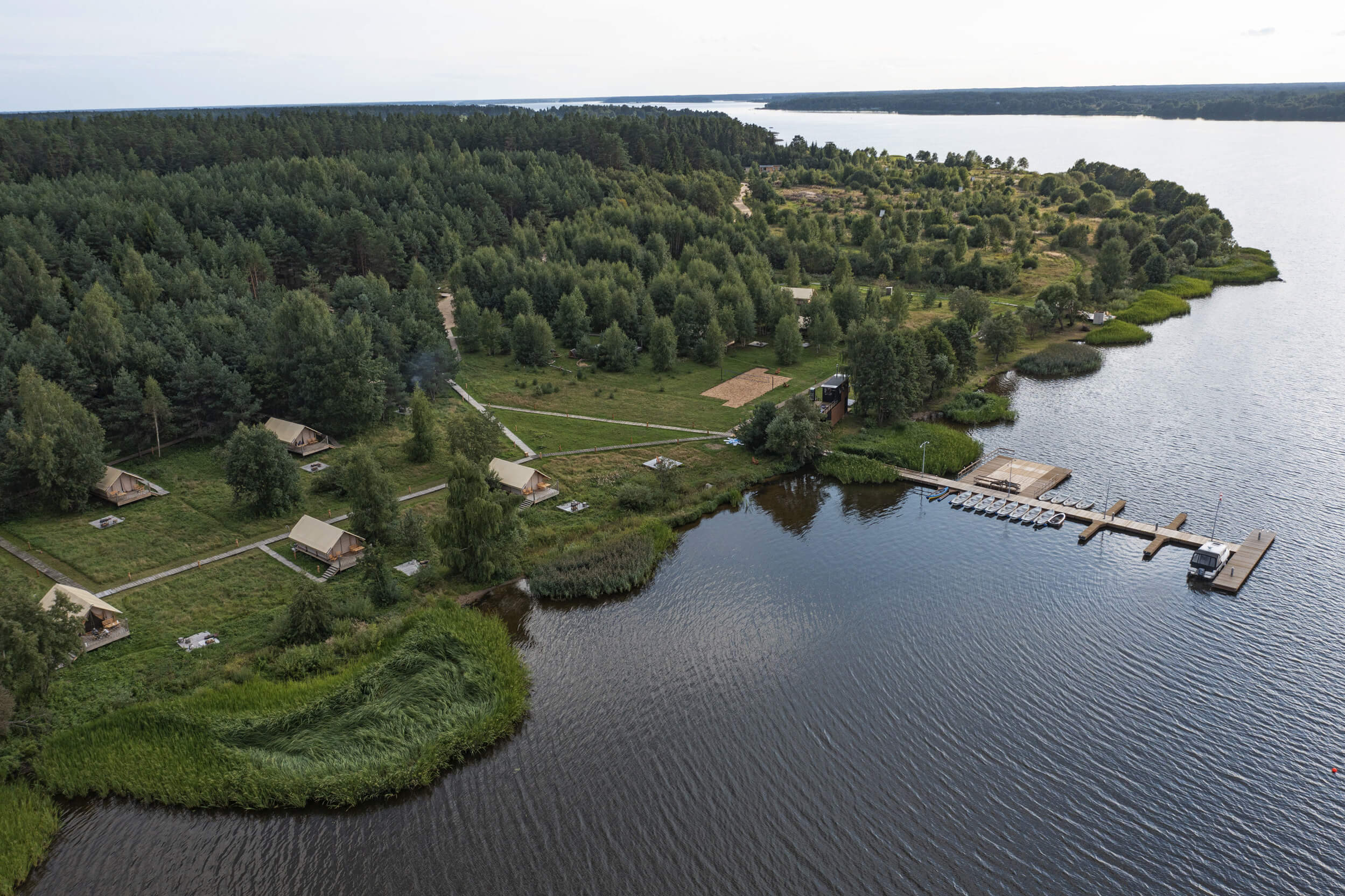 Панорамный вид: река и лес, пирс с лодками, на берегу - палатки для отдыха.